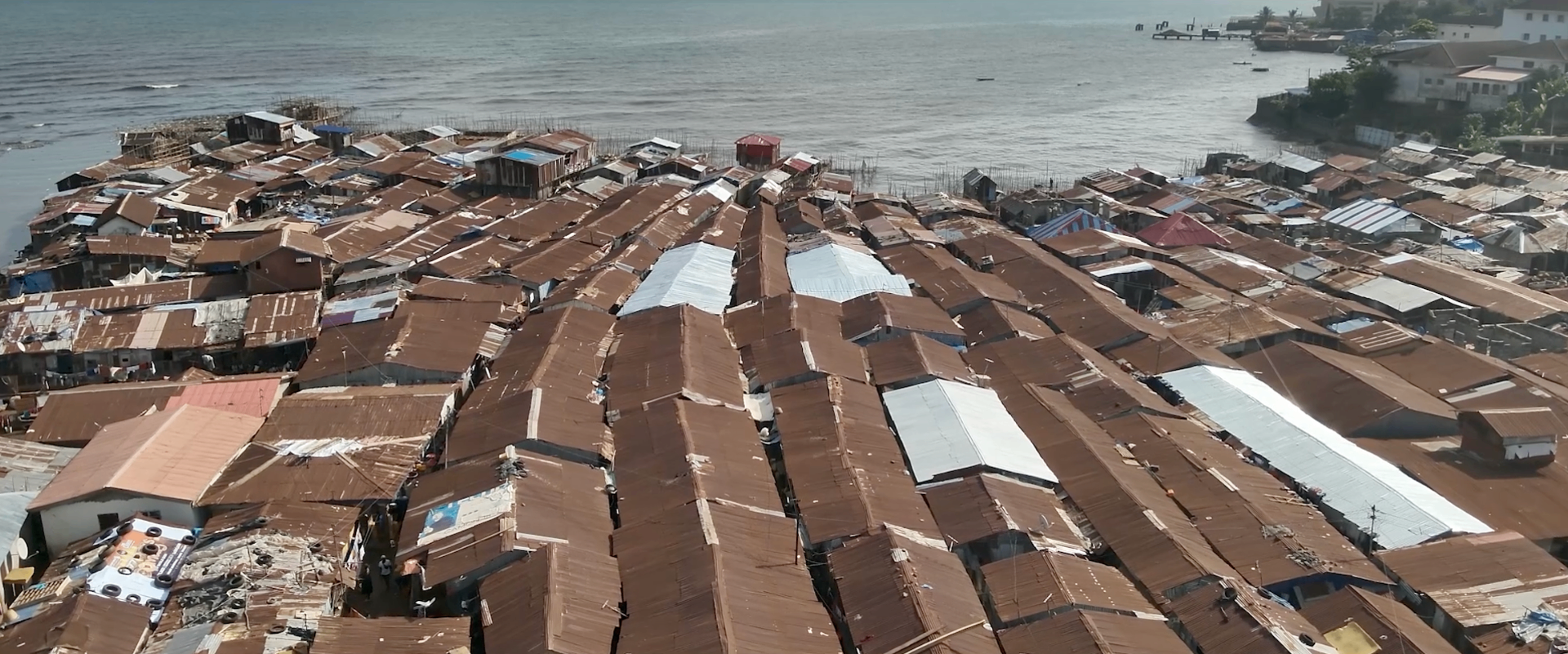 Aerial view of Kroo Bay, Sierra Leone, showing reflective MEER roofs installed among rusted metal rooftops next to the water